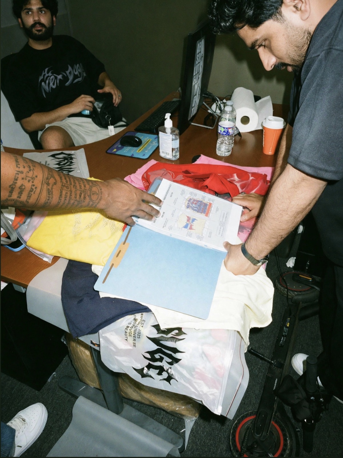 Design team reviewing a CRSVGE tech pack over a table of sample garments